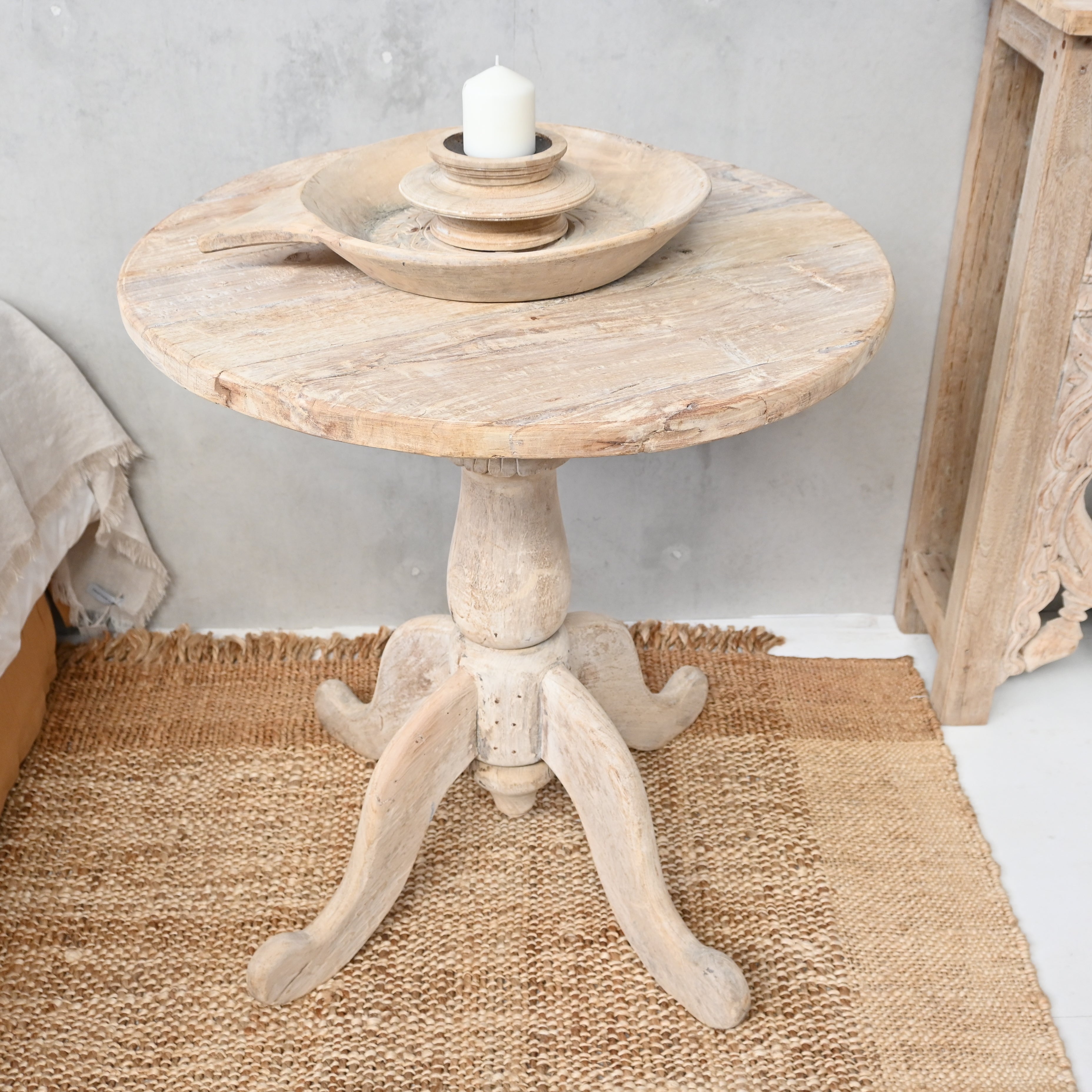 Round wooden side table with a candle on a textured rug
