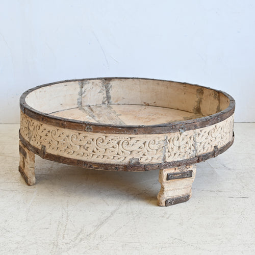 Decorative round wooden table with intricate carvings on a light background