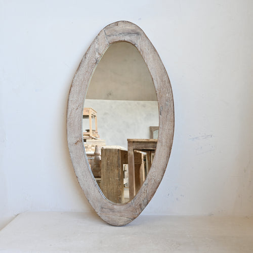 Oval mirror with wooden frame on a white surface