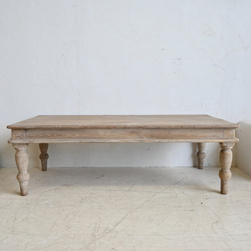 Wooden table with turned legs on a light wooden floor against a white wall