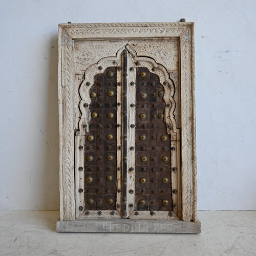 Decorative wooden window with intricate carvings and brass studs on a white background