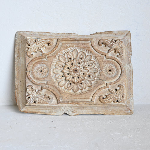Decorative wooden panel with intricate carvings on a light gray background
