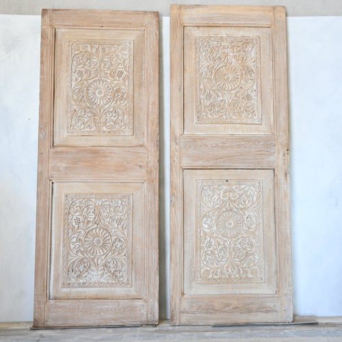 Pair of wooden doors with intricate carvings on a white wall.