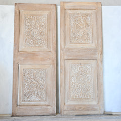 Pair of wooden doors with intricate carvings on a white wall.