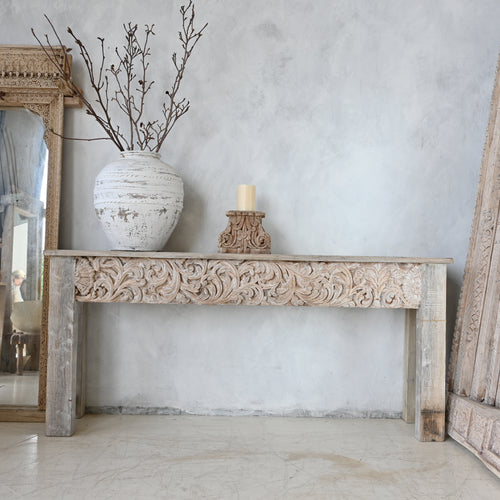 Carved wooden console table with decorative items against a light gray wall.