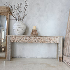 Carved wooden console table with decorative items against a light gray wall.