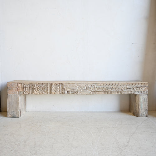 Carved wooden bench against a white wall