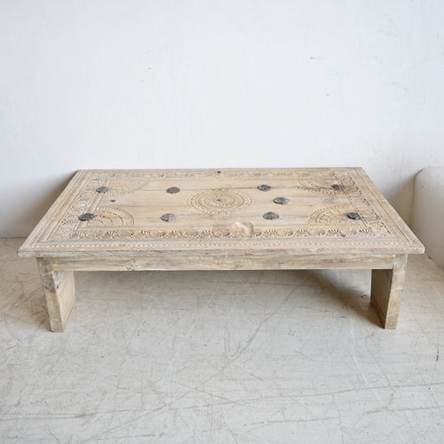 Wooden coffee table with intricate carvings on a white floor and wall
