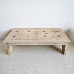 Wooden coffee table with intricate carvings on a white floor and wall