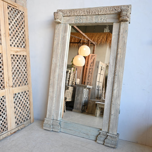 Large ornate mirror with wooden frame in a room with wooden lattice door.