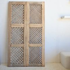 Wooden lattice door panel with intricate patterns on a white wall.