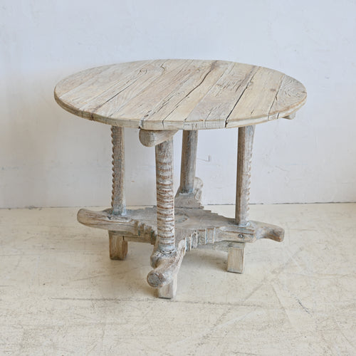 Round wooden table with rustic legs on a white floor and wall
