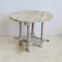 Round wooden table with rustic legs on a white floor and wall